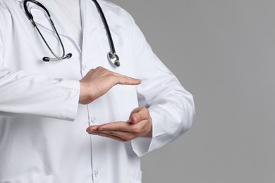 Photo of Doctor holding something on grey background, closeup. Space for text