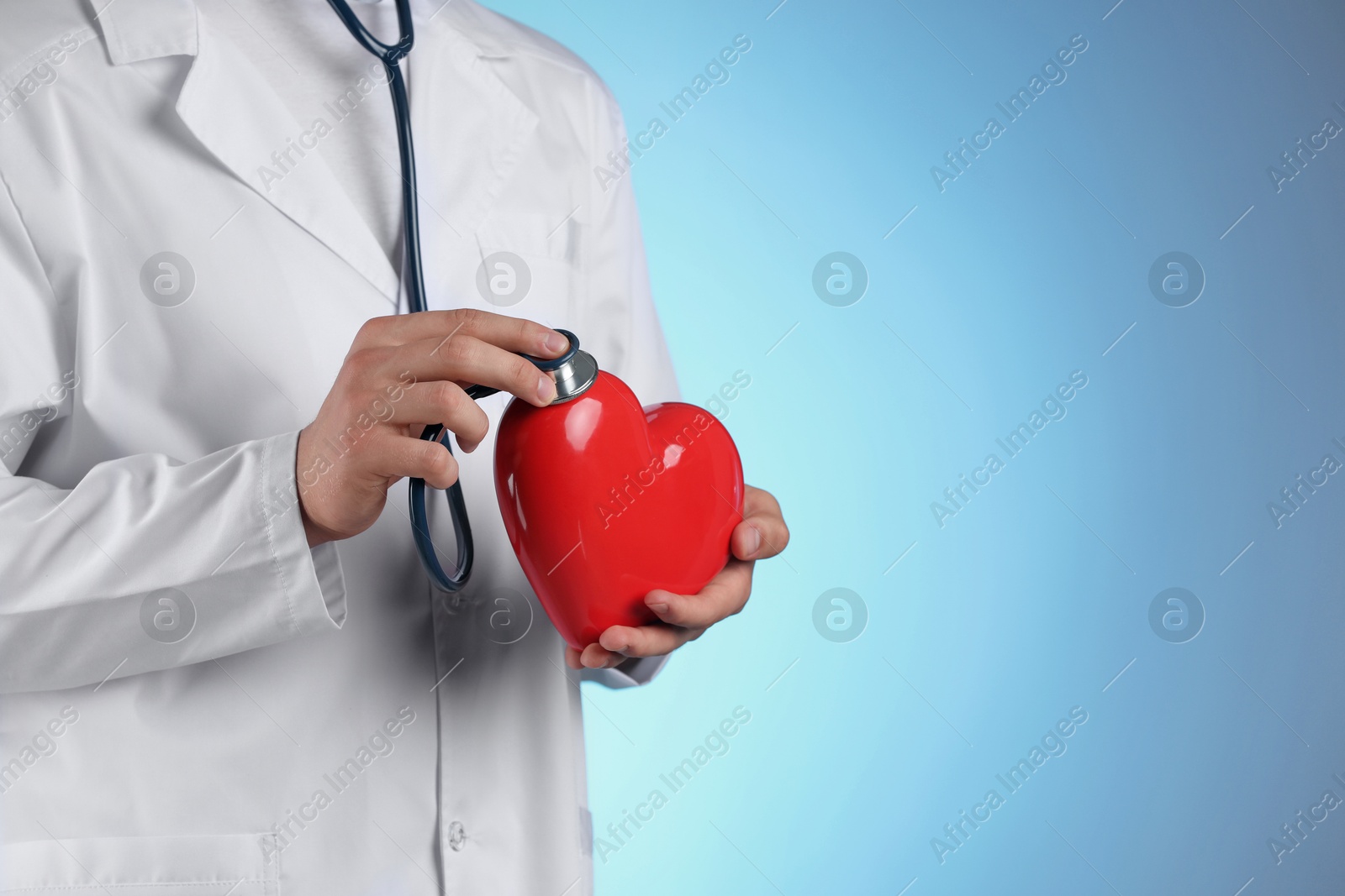 Photo of Doctor with stethoscope and red heart on light blue background, closeup. Space for text