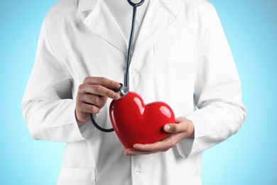 Doctor with stethoscope and red heart on light blue background, closeup