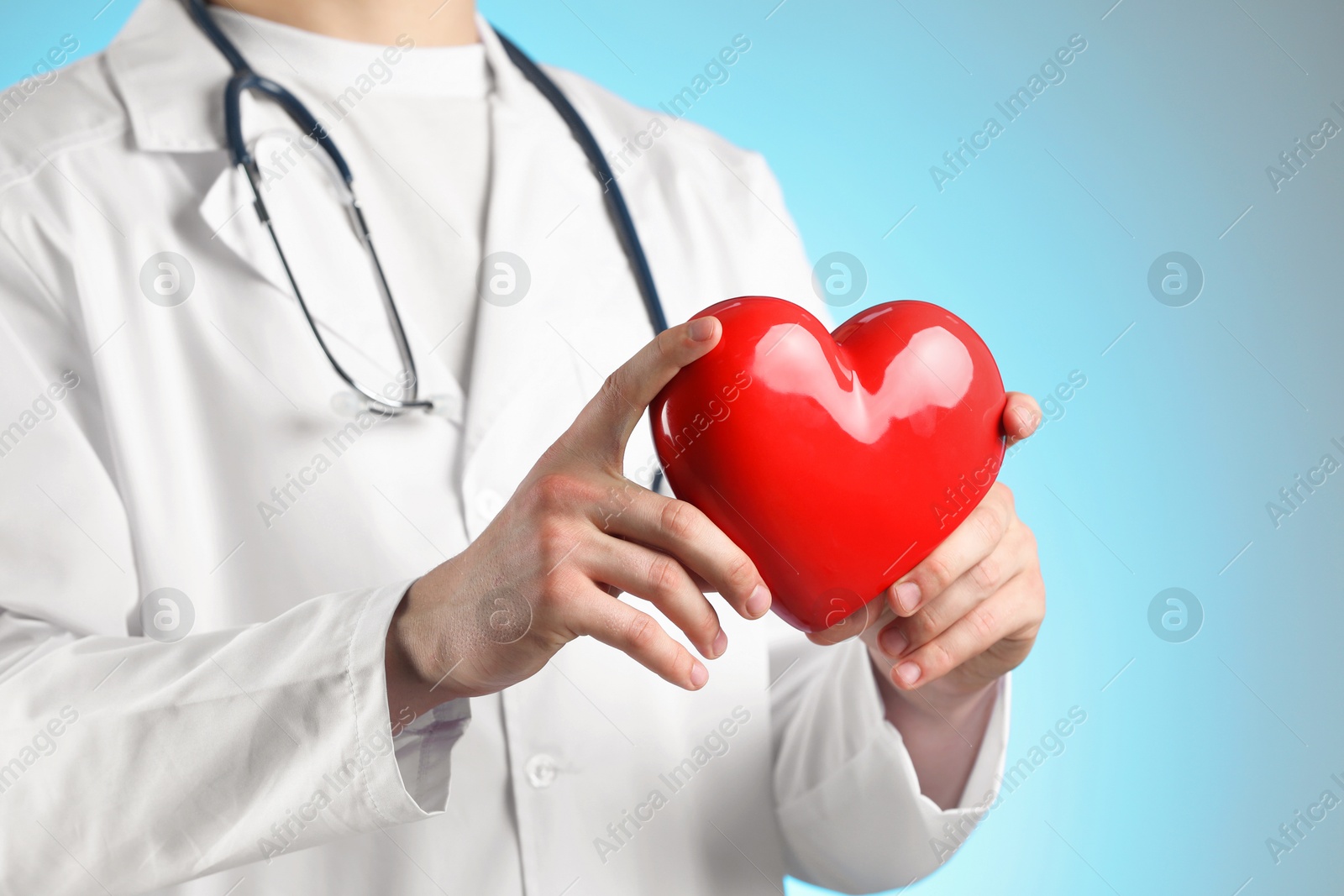 Photo of Doctor with red heart on light blue background, closeup