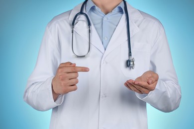 Photo of Doctor pointing at something on light blue background, closeup