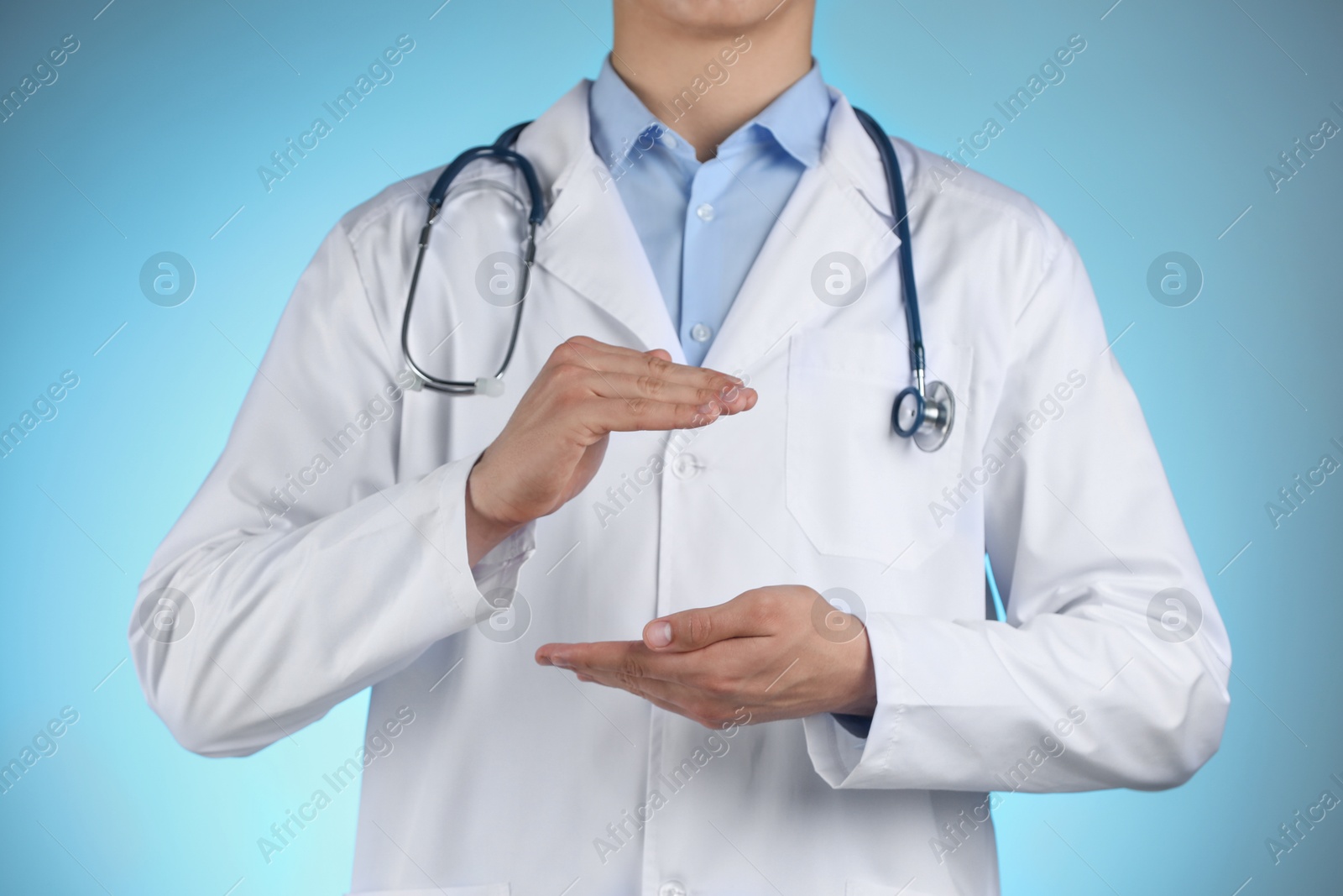 Photo of Doctor holding something on light blue background, closeup