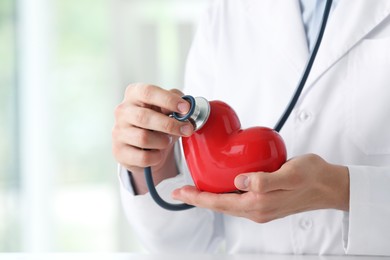 Photo of Doctor with stethoscope and red heart indoors, closeup