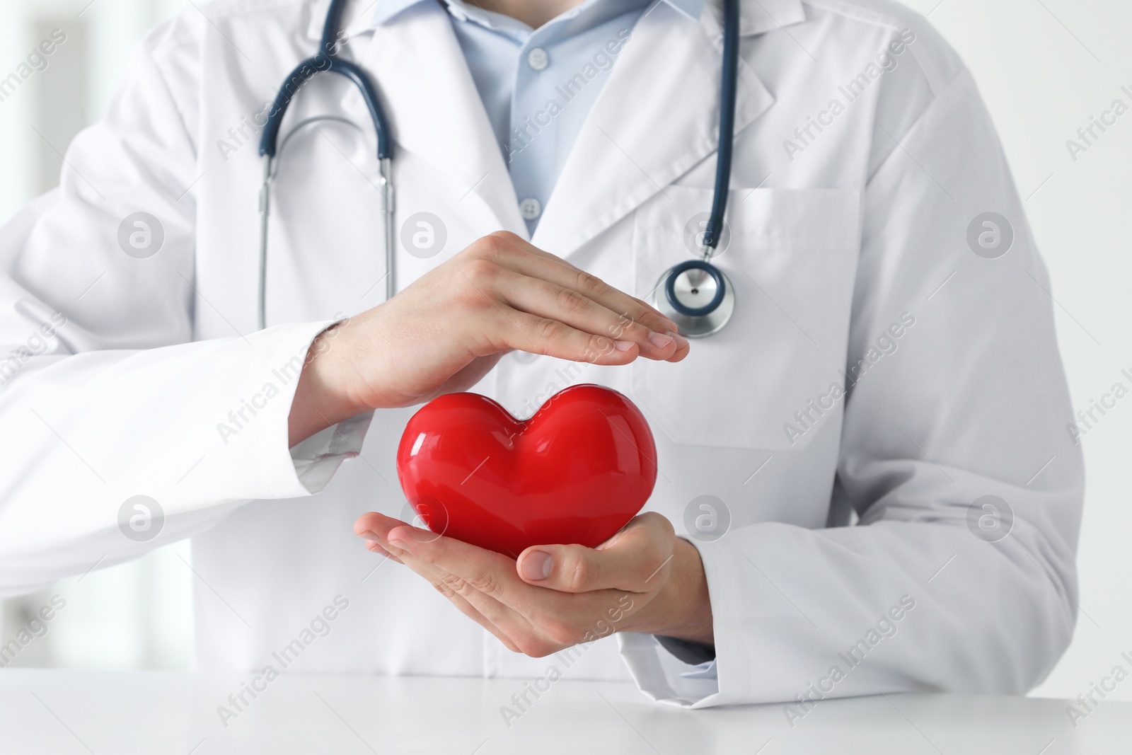 Photo of Doctor with red heart at white table in clinic, closeup