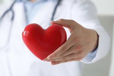 Doctor with red heart indoors, selective focus