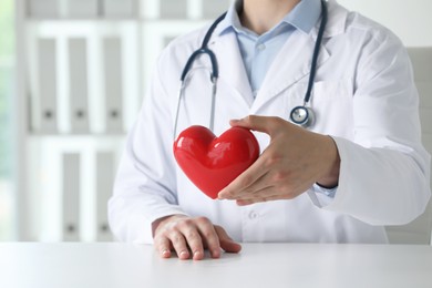 Doctor with red heart at white table in clinic, closeup