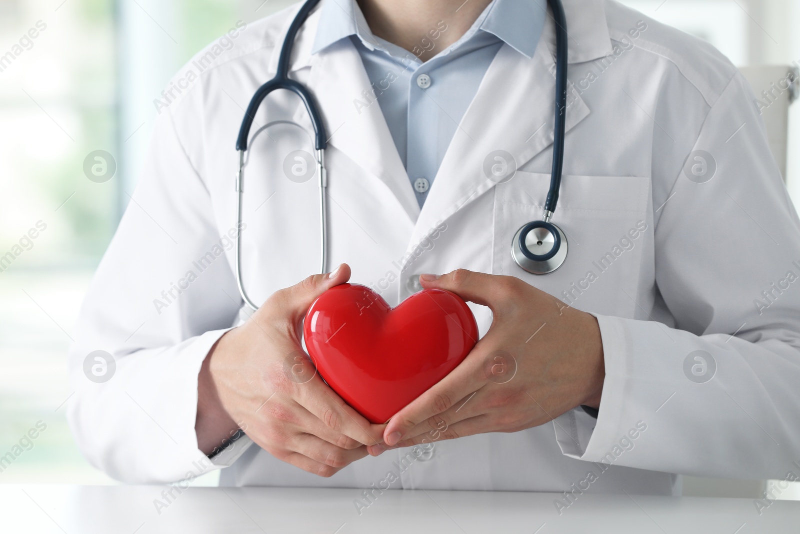 Photo of Doctor with red heart at white table in clinic, closeup