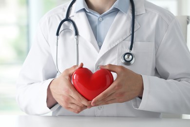 Photo of Doctor with red heart at white table in clinic, closeup