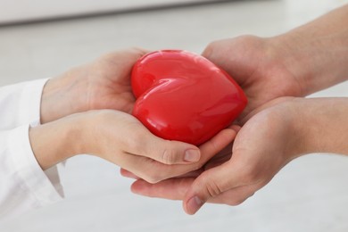 Doctor giving red heart to patient at white table in clinic, closeup