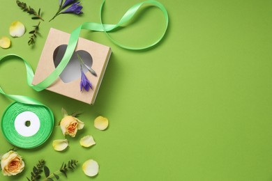 Photo of Flat lay composition with beautiful ribbon reel and gift box on green background, space for text