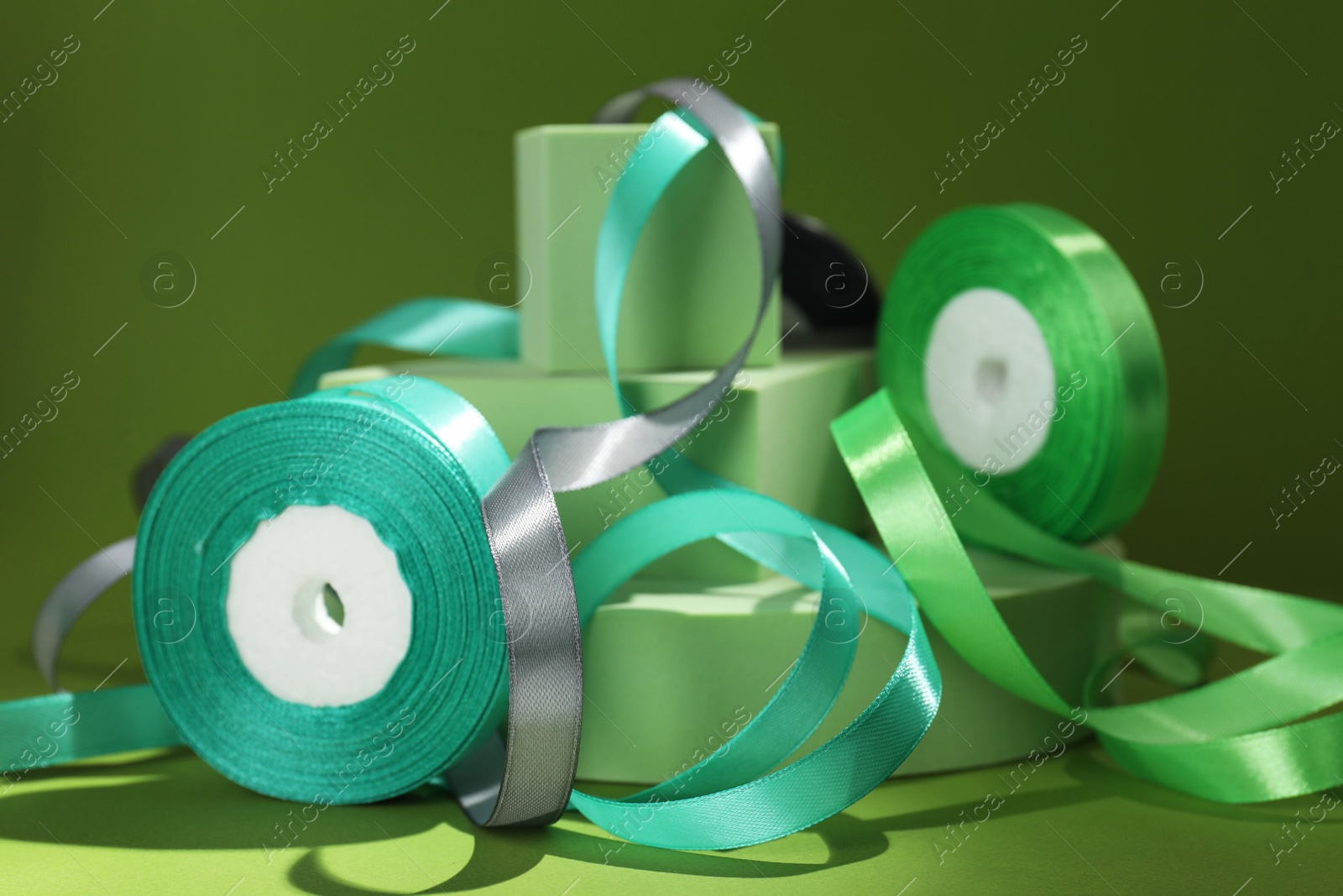 Photo of Beautiful ribbon reels and different podiums on green background, closeup