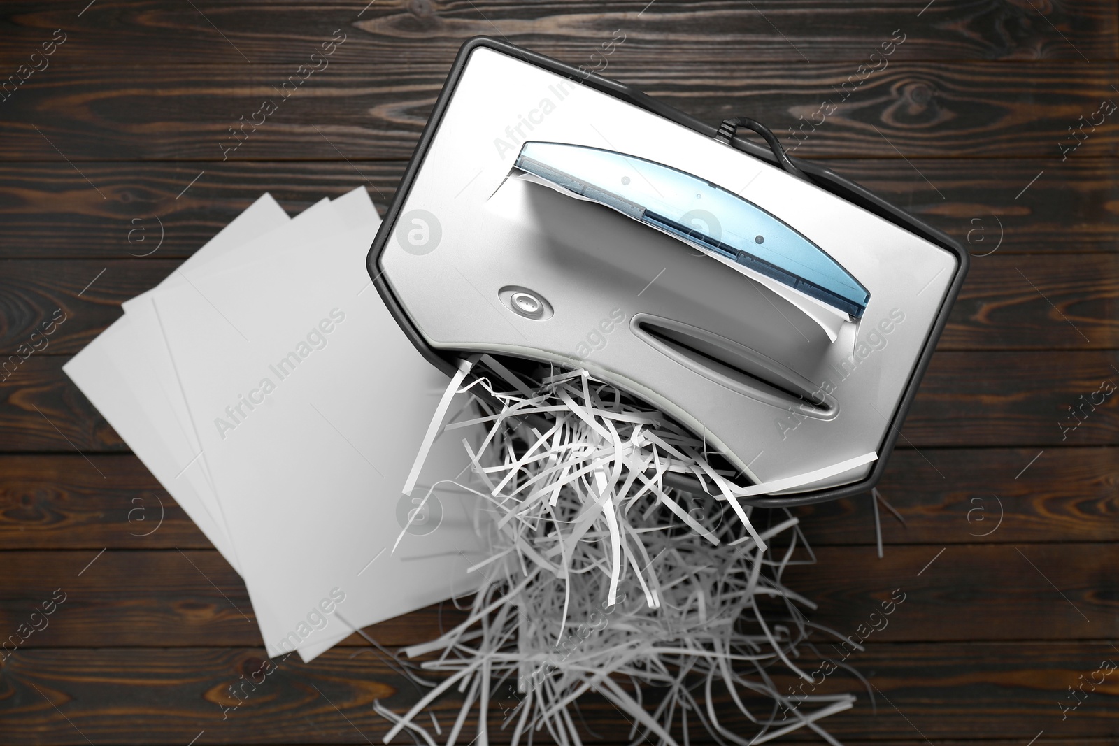 Photo of Shredder, trash bin, paper strips and sheets on wooden table, flat lay