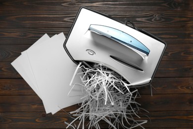 Photo of Shredder, trash bin, paper strips and sheets on wooden table, flat lay