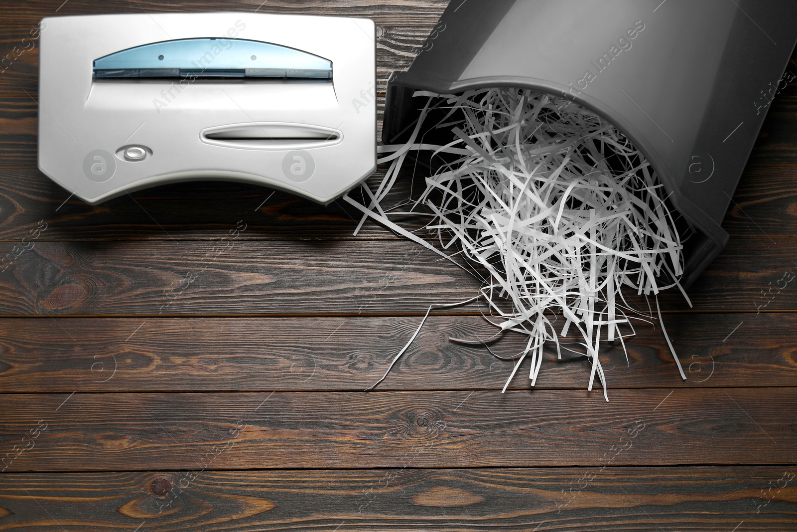 Photo of Shredder, black bin and paper strips on wooden table, flat lay. Space for text