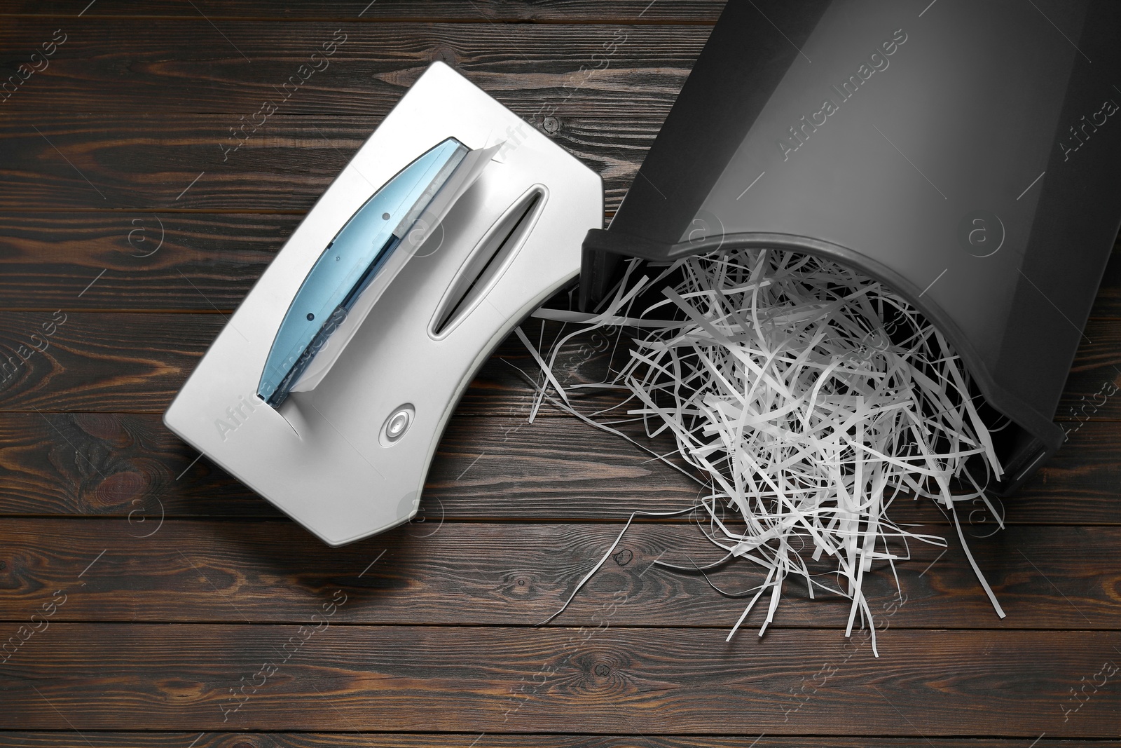 Photo of Shredder, black bin and paper strips on wooden table, flat lay