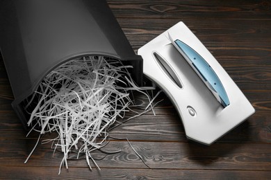 Shredder, black bin and paper strips on wooden table, flat lay