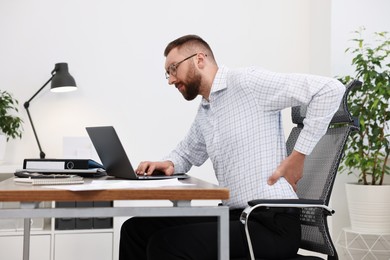 Photo of Man suffering from back pain in office. Symptom of poor posture