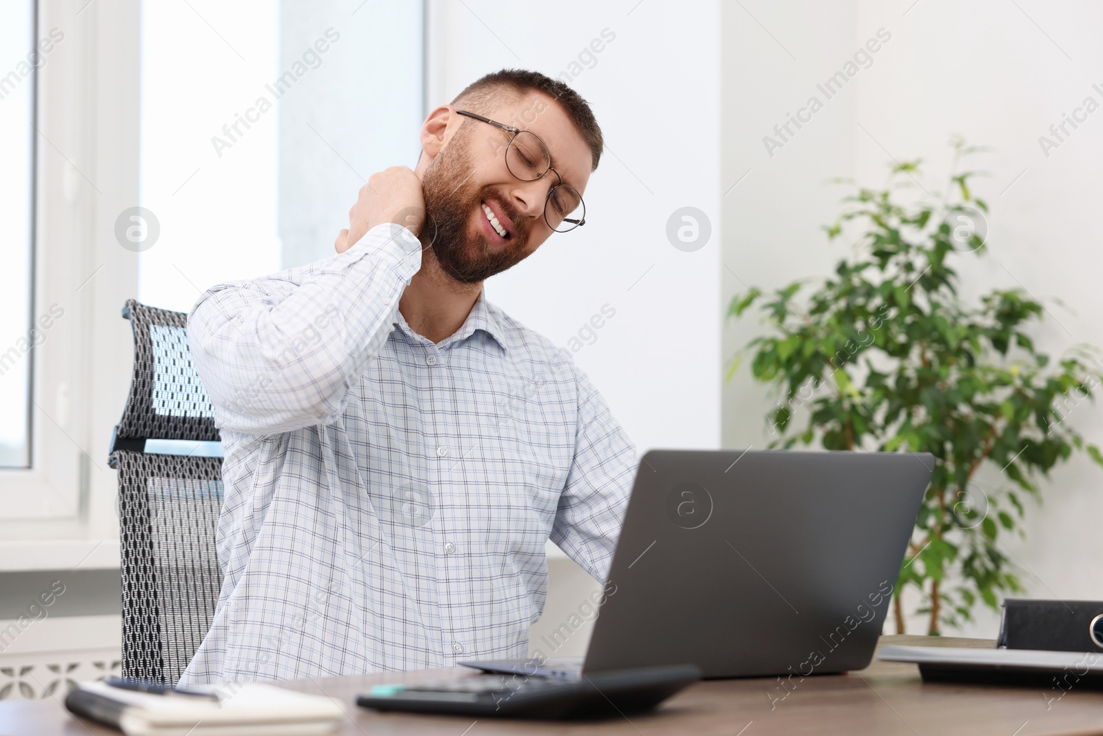 Photo of Man suffering from neck pain in office. Symptom of poor posture