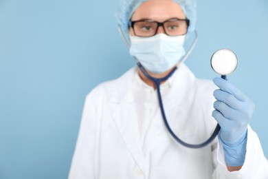 Photo of Doctor holding stethoscope on light blue background, selective focus