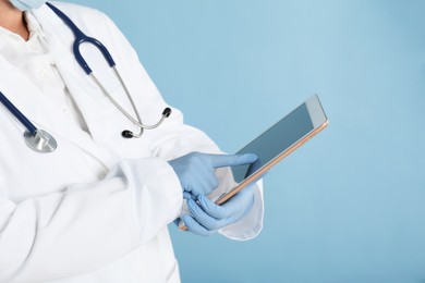 Doctor with tablet on light blue background, closeup view