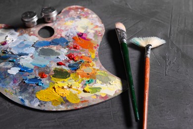 Artist's palette, brushes and paints on grey table, closeup