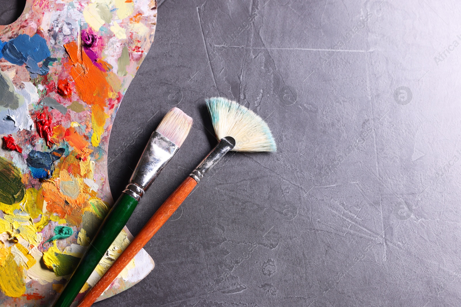 Photo of Artist's palette, brushes and paints on grey table, flat lay. Space for text