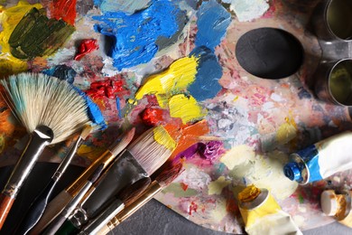 Photo of Artist's palette, brushes and paints on grey table, flat lay