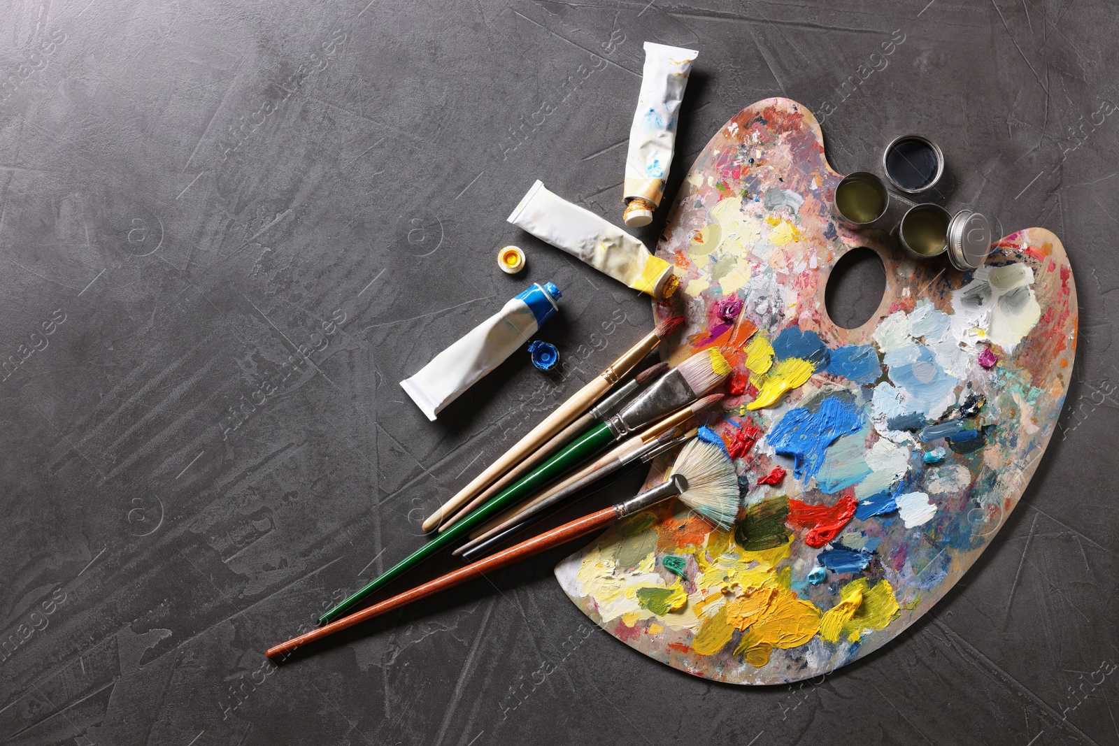 Photo of Artist's palette, brushes and paints on grey table, flat lay. Space for text