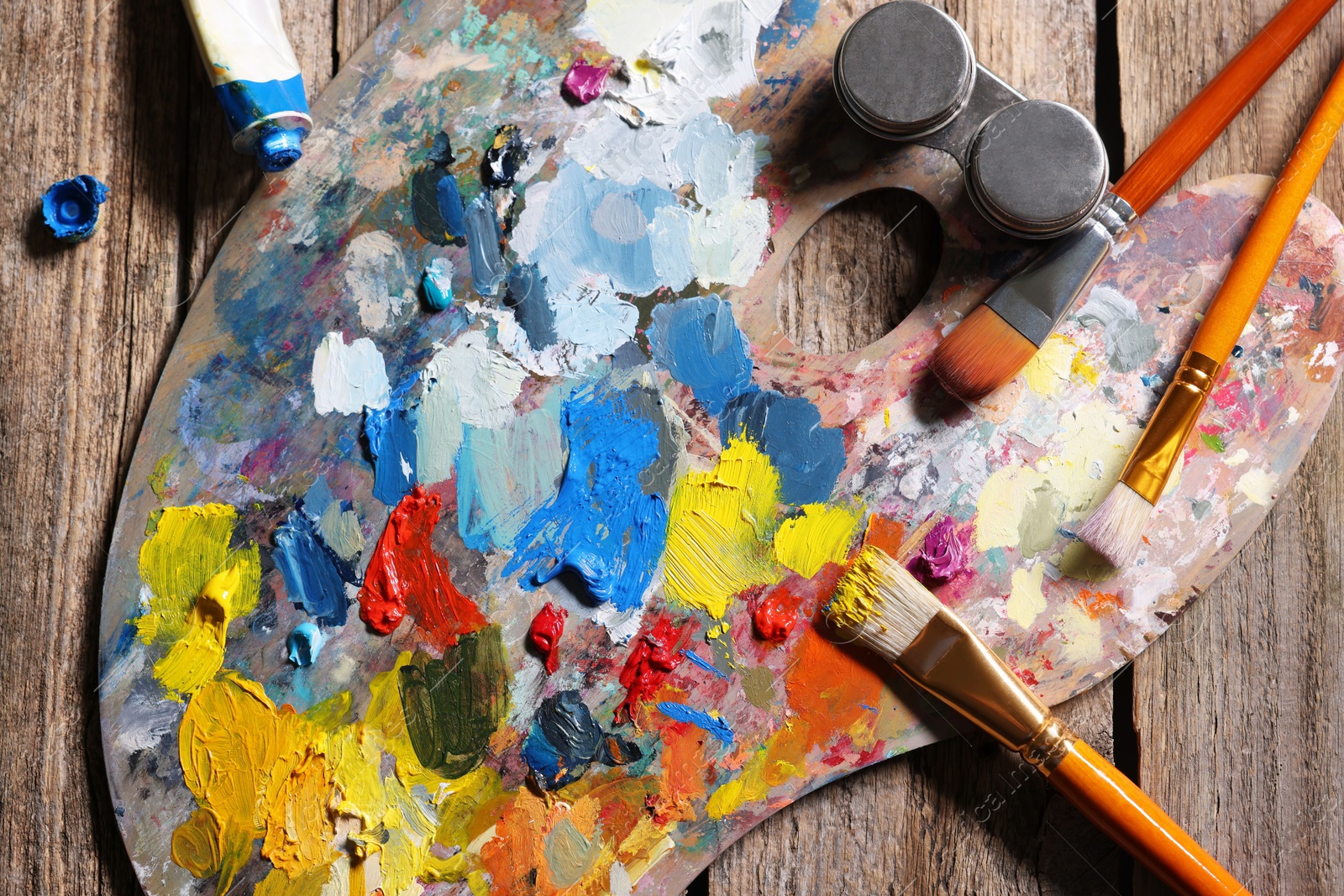 Photo of Artist's palette, brushes and paints on wooden table, flat lay