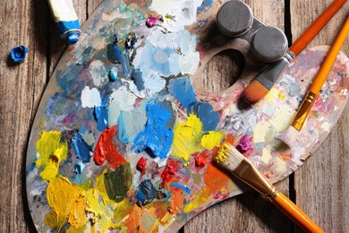 Artist's palette, brushes and paints on wooden table, flat lay