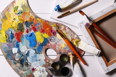 Photo of Artist's palette, brushes, paints and blank canvases on white wooden table, flat lay