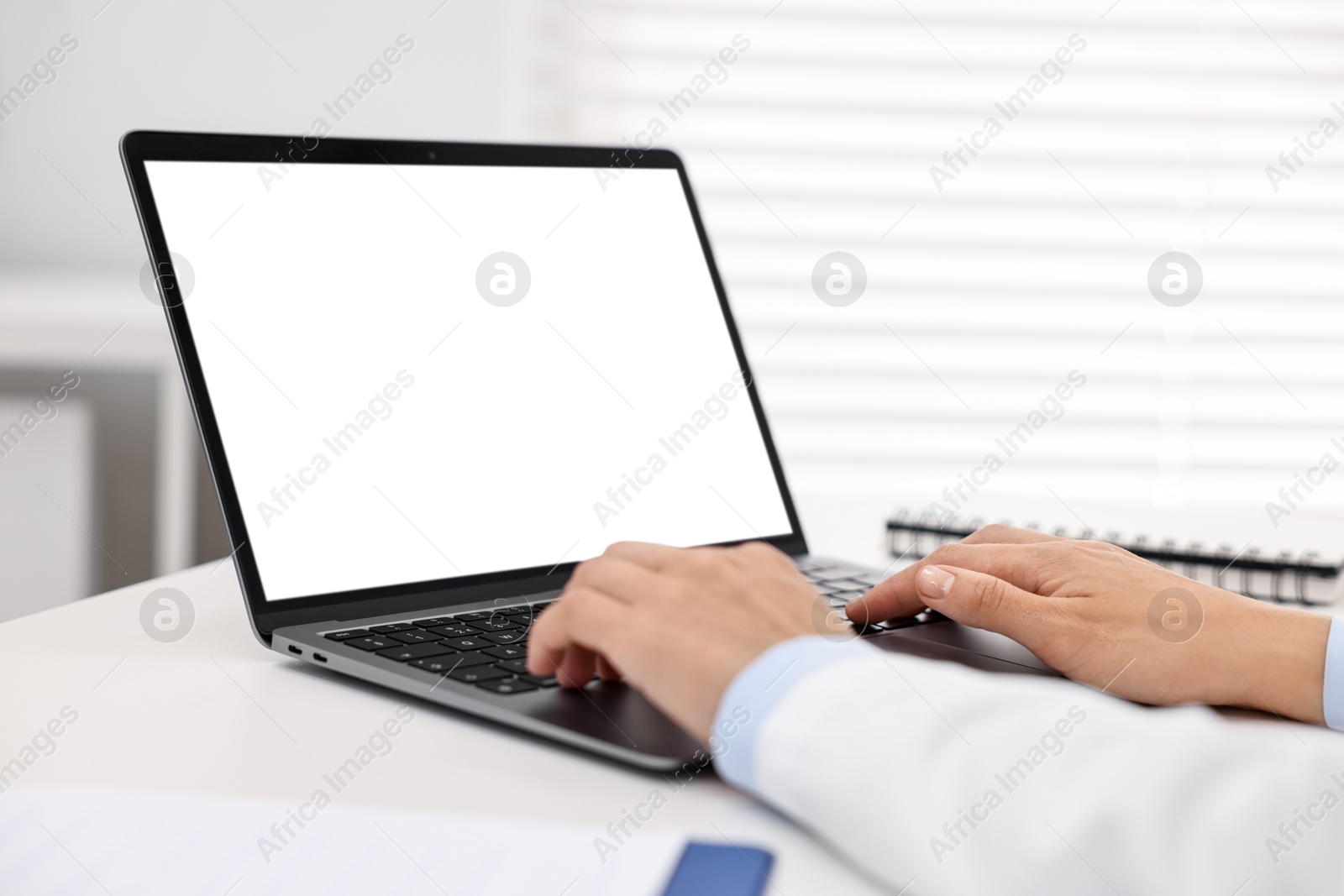 Photo of Doctor using laptop at white table in hospital, closeup