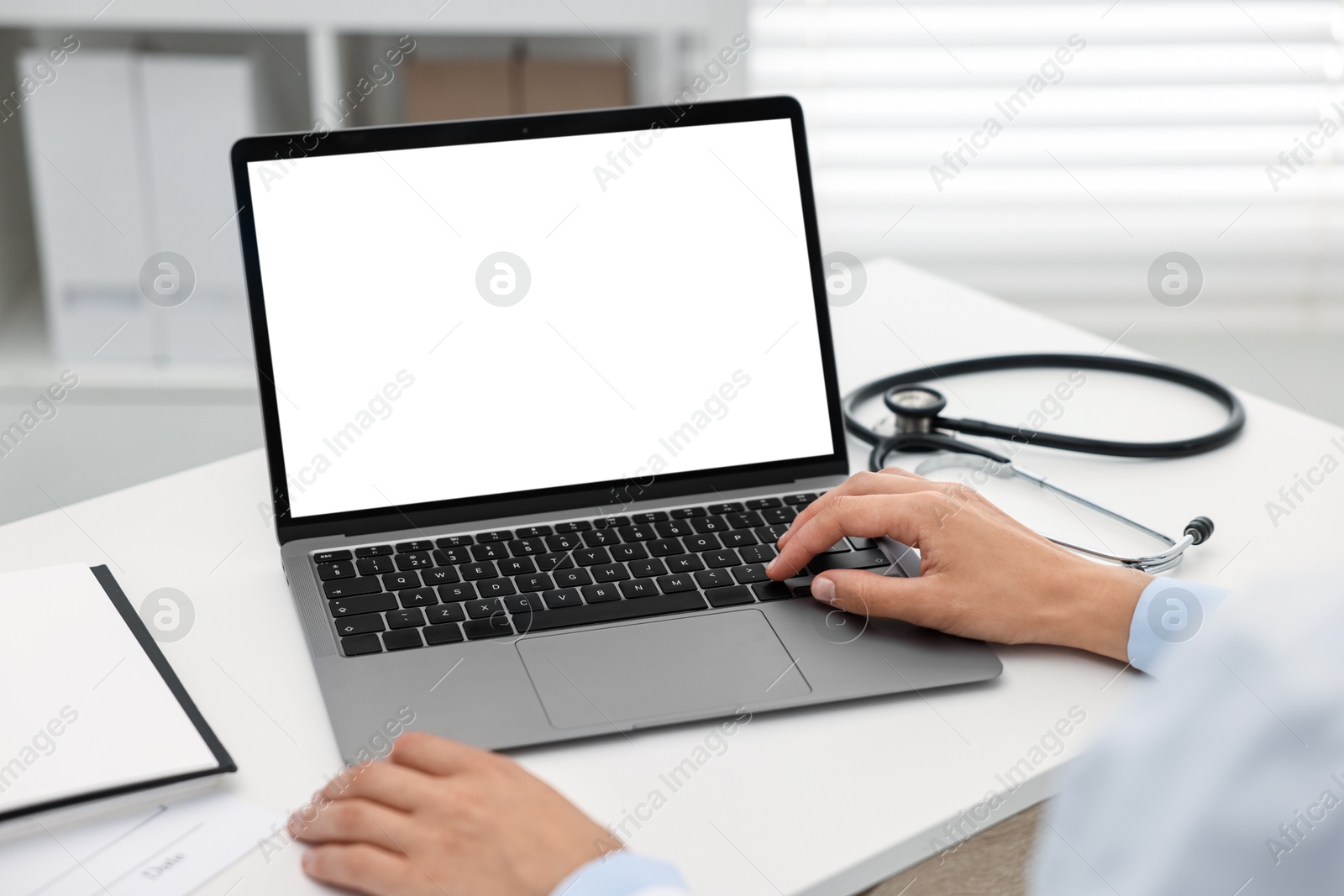 Photo of Doctor using laptop at white table in hospital, closeup