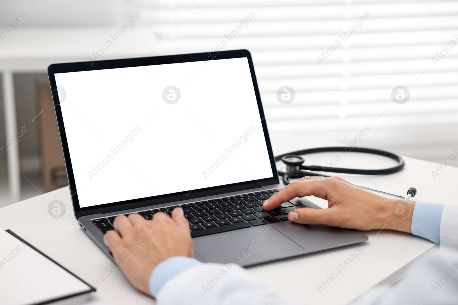 Photo of Doctor using laptop at white table in hospital, closeup