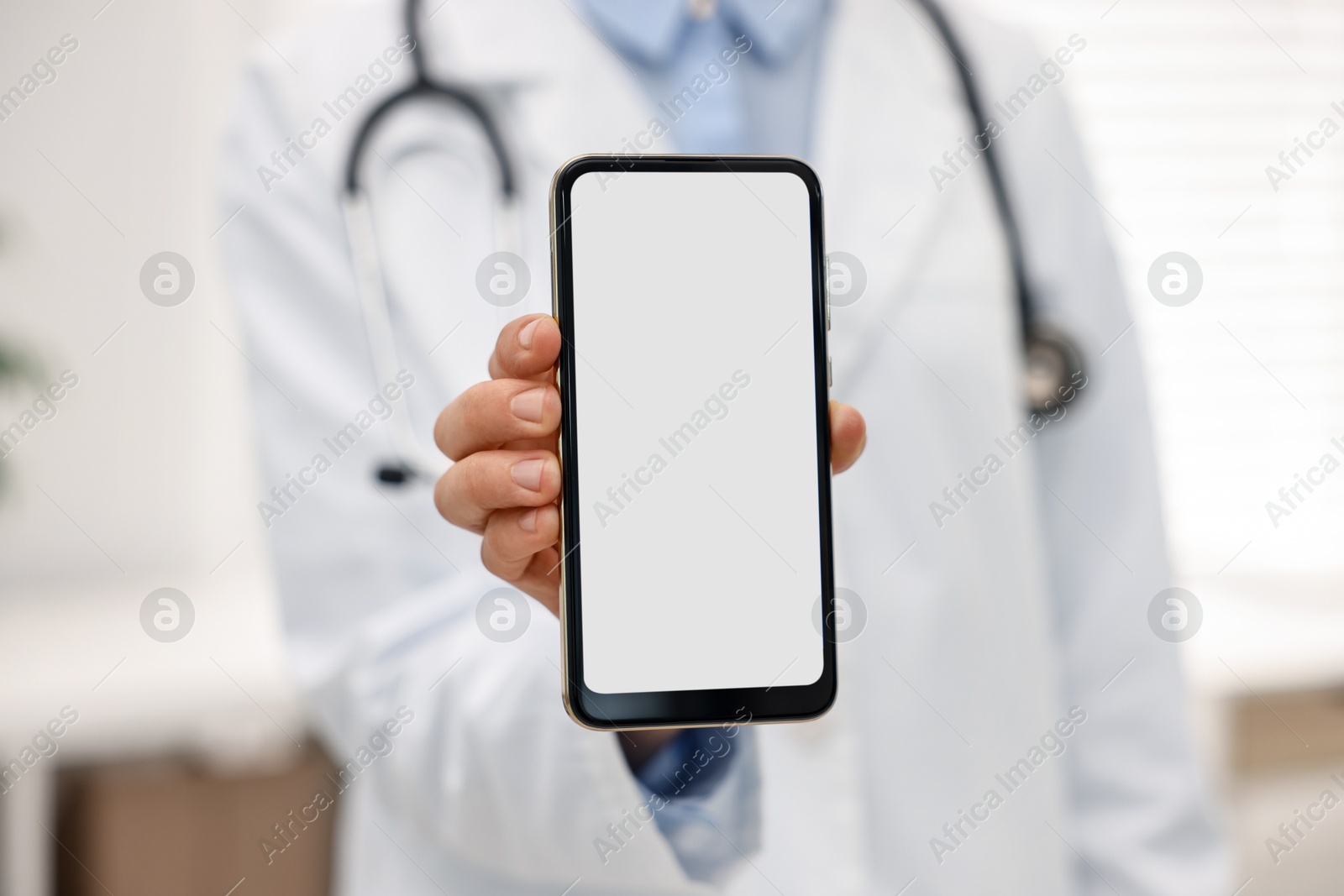 Photo of Doctor showing smartphone with blank screen in hospital, selective focus