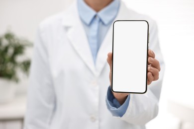 Photo of Doctor showing smartphone with blank screen in hospital, selective focus