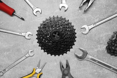 Wrenches, pliers, bicycle tire, cassette and chain on grey textured background, flat lay