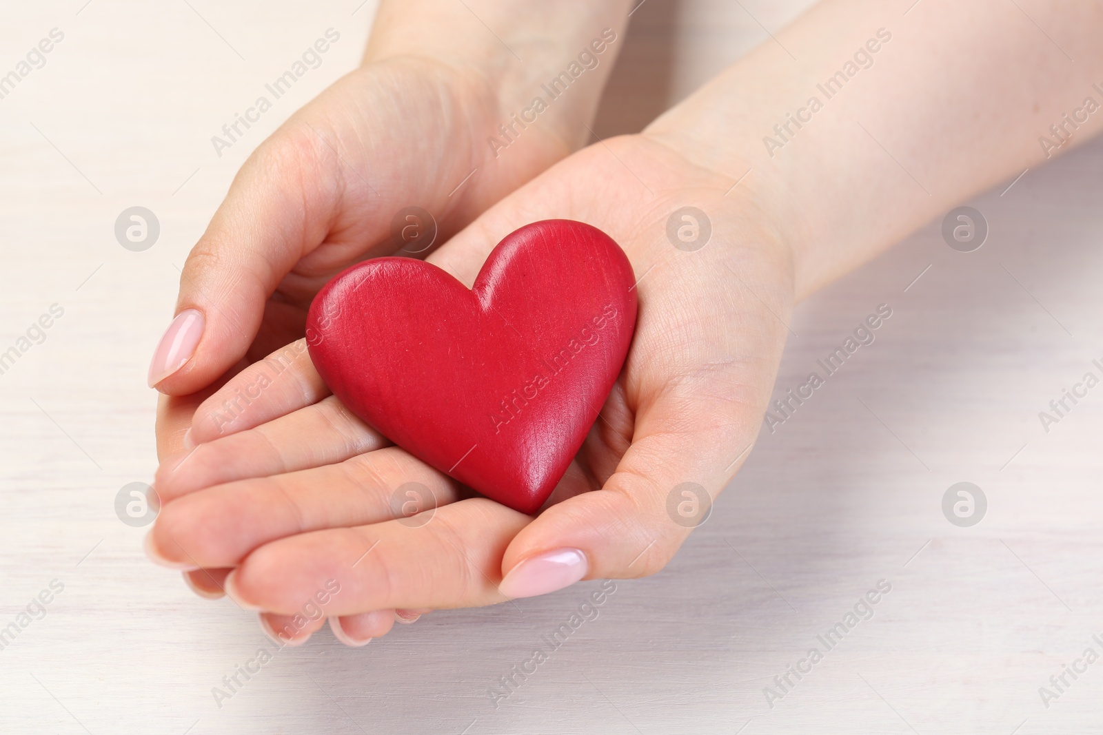 Photo of Woman with red decorative heart at white wooden table, closeup