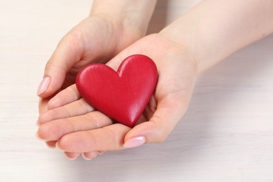 Photo of Woman with red decorative heart at white wooden table, closeup