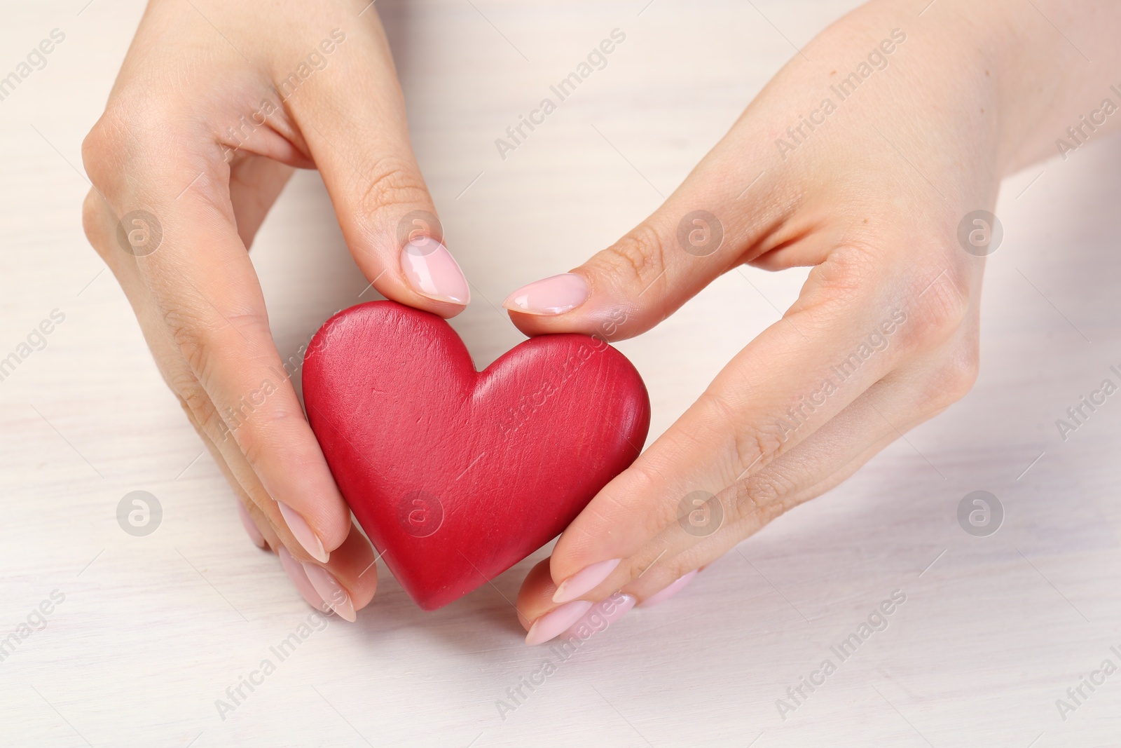 Photo of Woman with red decorative heart at white wooden table, closeup