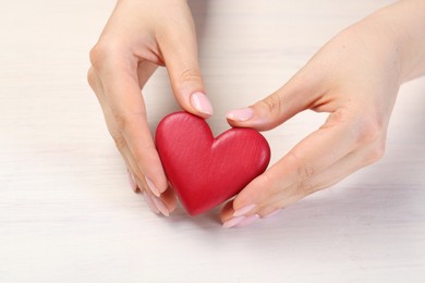 Photo of Woman with red decorative heart at white wooden table, closeup