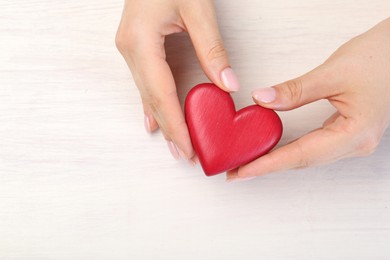 Woman with red decorative heart at white wooden table, top view. Space for text