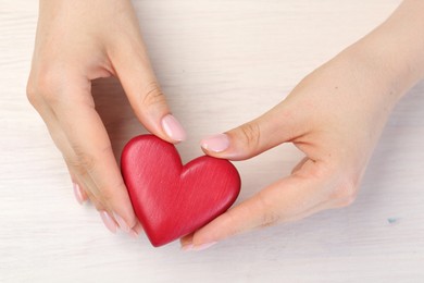 Woman with red decorative heart at white wooden table, top view