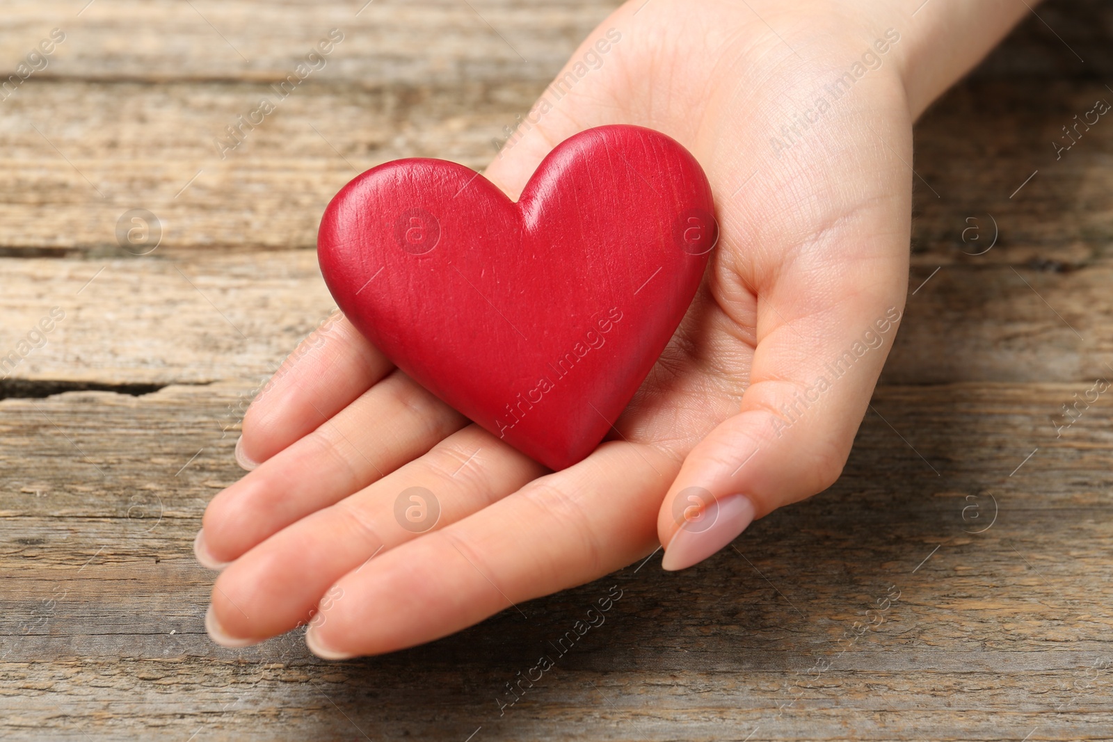 Photo of Woman with red decorative heart at wooden table, closeup