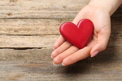 Photo of Woman with red decorative heart at wooden table, closeup. Space for text