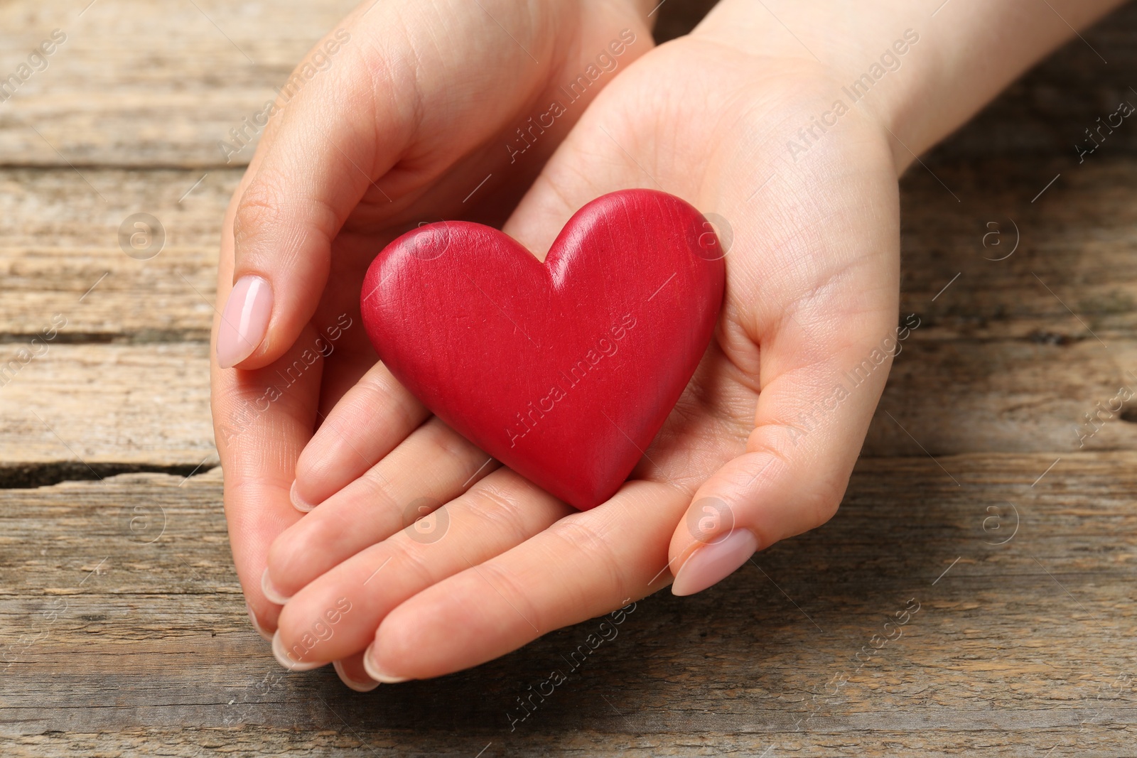 Photo of Woman with red decorative heart at wooden table, closeup