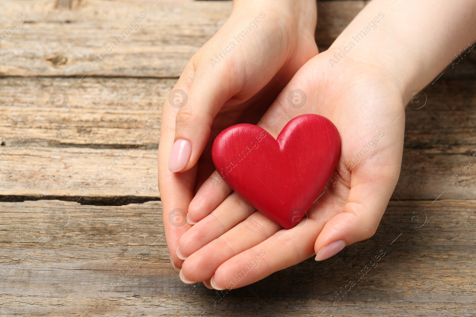 Photo of Woman with red decorative heart at wooden table, closeup