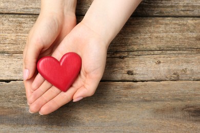 Photo of Woman with red decorative heart at wooden table, top view. Space for text