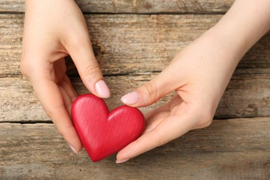 Photo of Woman with red decorative heart at wooden table, top view