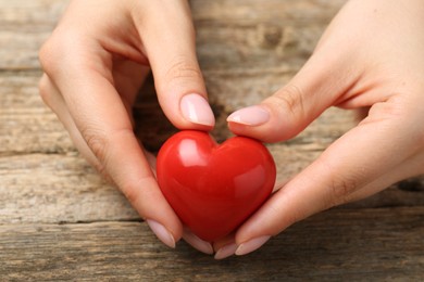 Woman with red decorative heart at wooden table, closeup